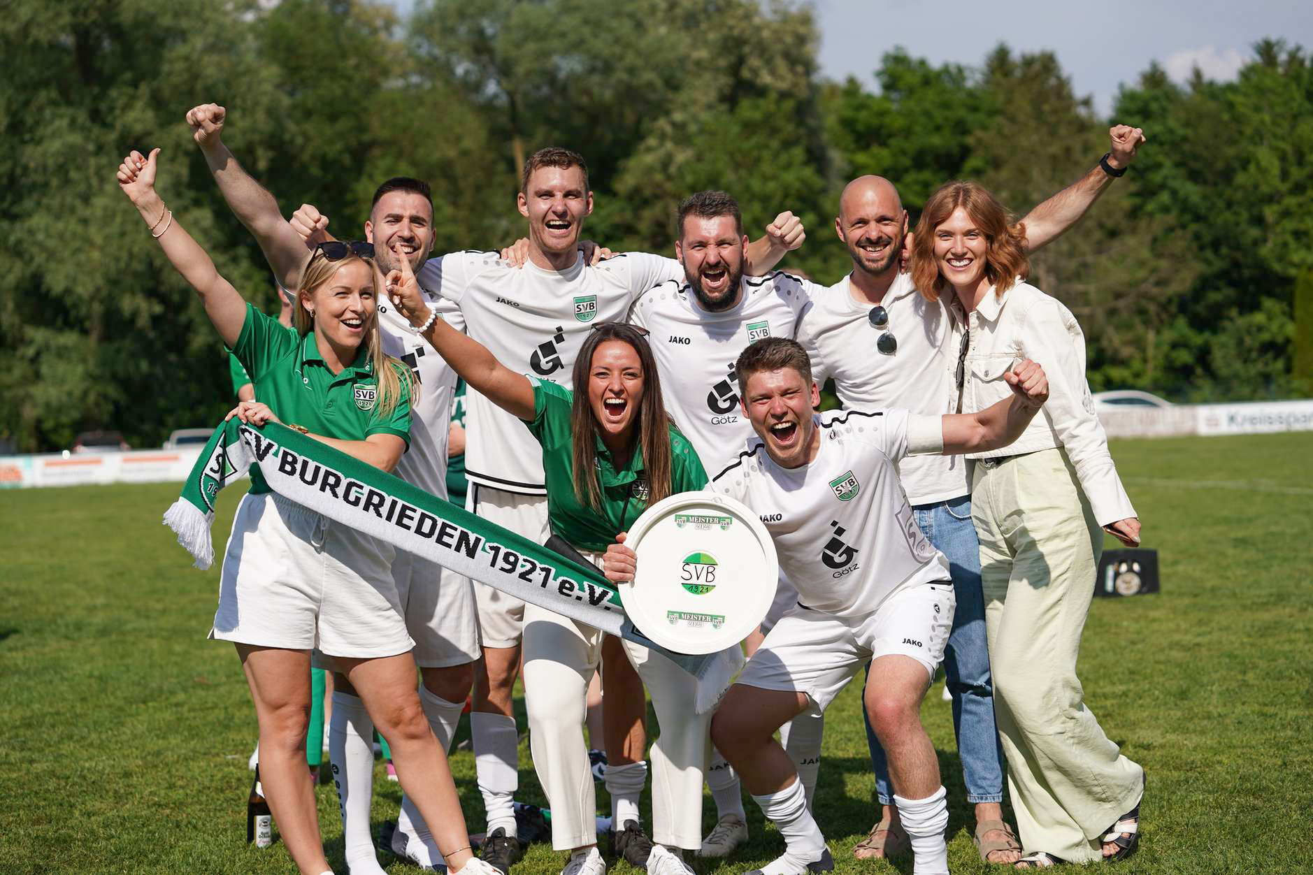 Eine Gruppe von Personen in Sportkleidung feiert auf einem Fußballfeld.
