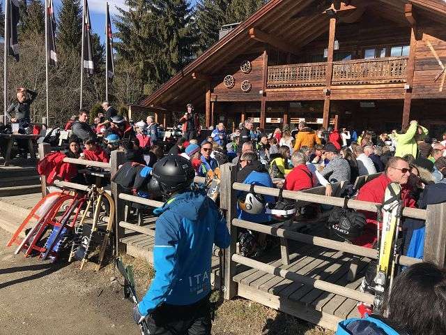 Viele Menschen sitzen in einer Ski-Lodge im Freien bei sonnigem Wetter.