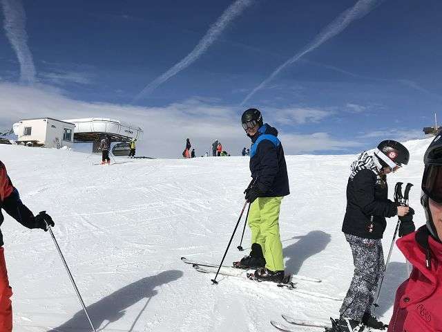 Menschen beim Skifahren auf einer verschneiten Piste unter blauem Himmel