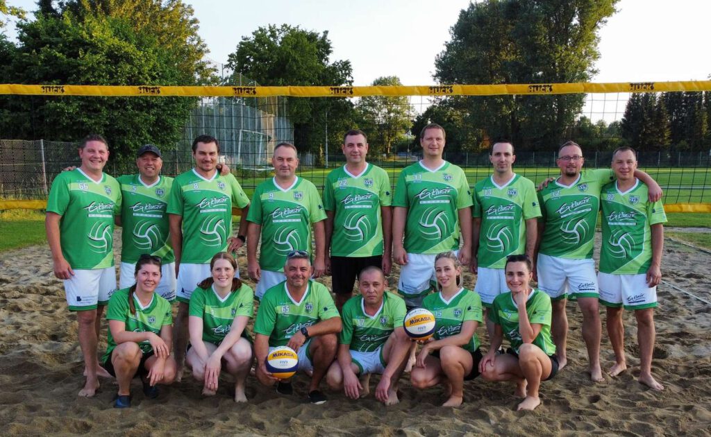Ein Volleyballteam in gruenen Trikots posiert auf einem Sandplatz.