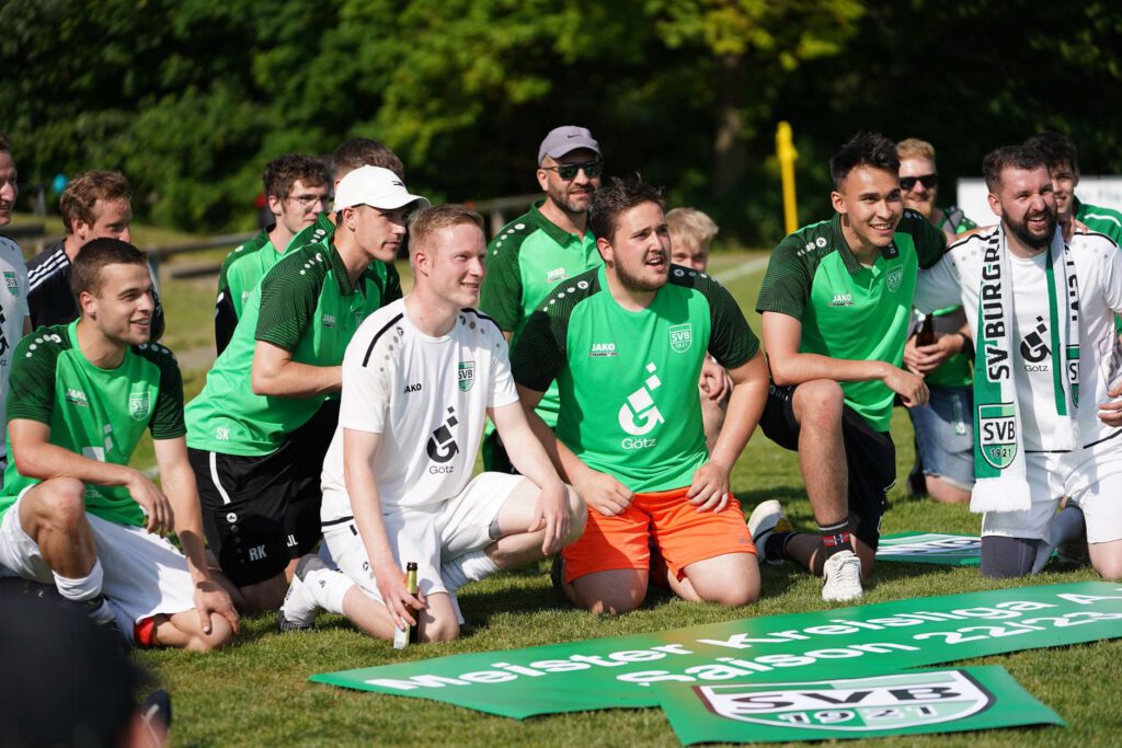 Eine Gruppe von Fußballfans in gruenen Trikots posiert auf einem Feld.