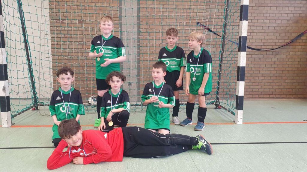 Ein Jugend-Fußballteam posiert in einer Sporthalle vor einem Tor.