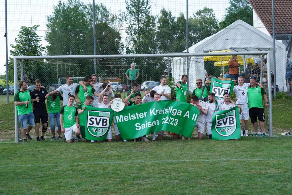 Eine Fußballmannschaft jubelt vor einem Tor mit gruenen Trikots und Transparenten.