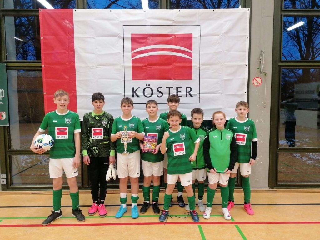 Junge Fußballmannschaft in gruenen Trikots in einer Sporthalle.