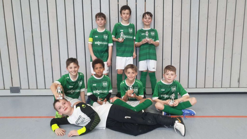 Eine Kinder-Fußballmannschaft posiert in einer Halle fuer ein Gruppenfoto.