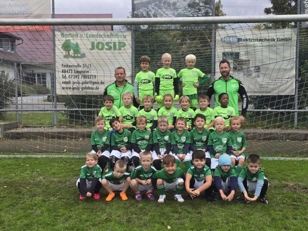 Eine Jugendfußballmannschaft posiert in gruenen Trikots auf einem Sportplatz.