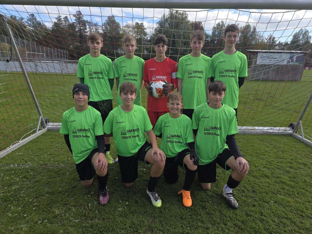 Eine Jugendfußballmannschaft posiert in gruenen Trikots auf einem Fußballfeld.
