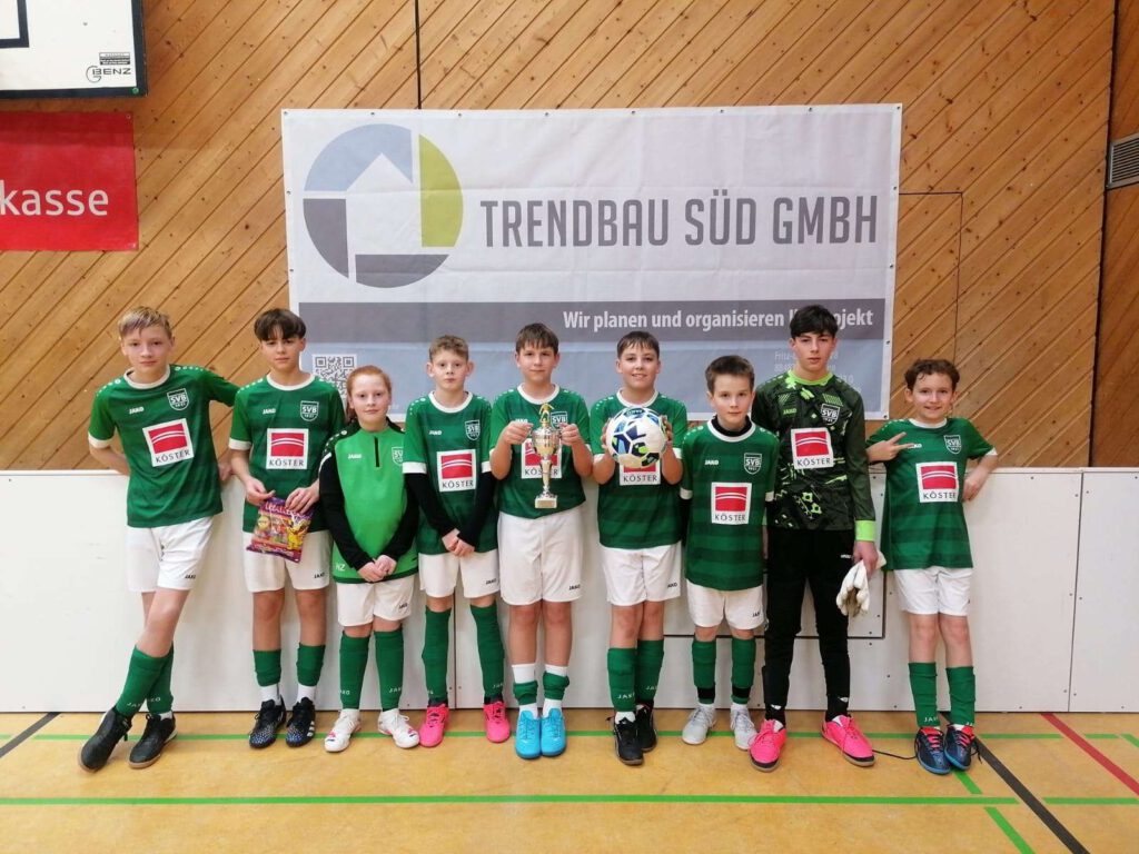 Eine Jugendfußballmannschaft steht in Trikots in einer Sporthalle.