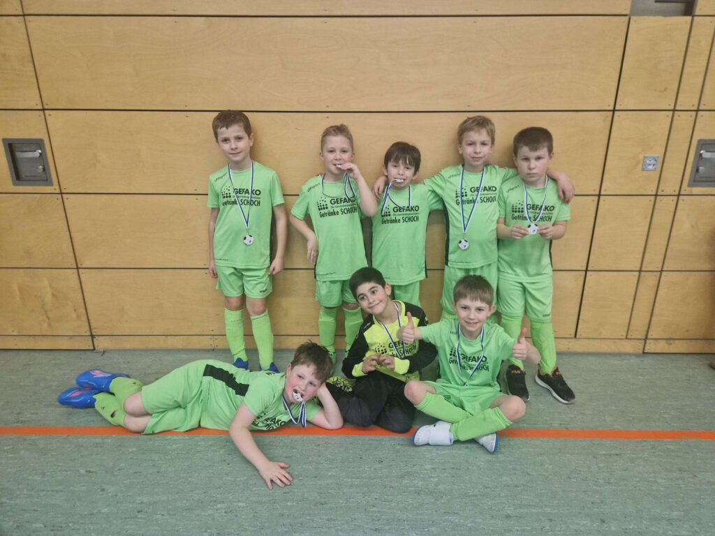 Eine Gruppe von Kindern in gruenen Sportoutfits posiert in einer Turnhalle.