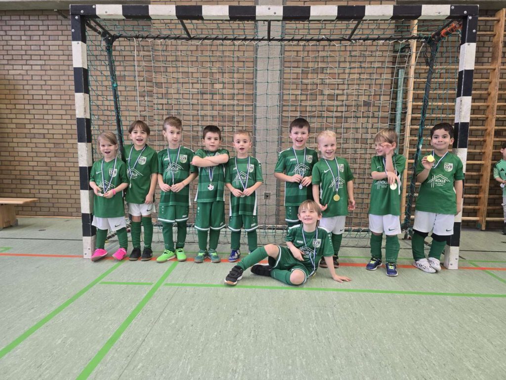 Eine Kinderfußballmannschaft posiert in gruenen Trikots vor einem Hallentor.