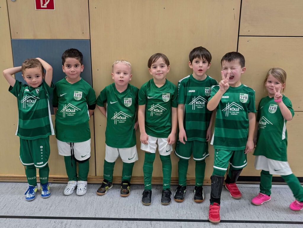 Eine Gruppe von Kindern in gruenen Fußballtrikots steht nebeneinander in einem Innenraum.