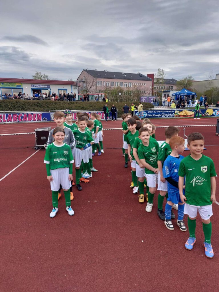 Kinder stehen in zwei Reihen auf einem Sportplatz waehrend eines Fußballturniers.
