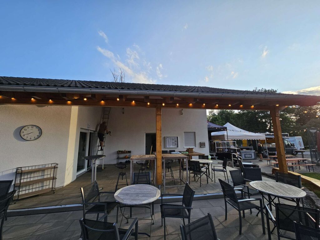 Ein gemuetliches Outdoor-Café mit Tischen und Stuehlen unter einer ueberdachten Terrasse.